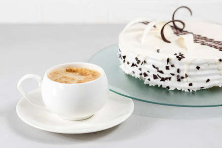 A cup of coffee and a white cake decorated with chocolate decor on a glass plate on a gray background. Selective focus.の写真素材