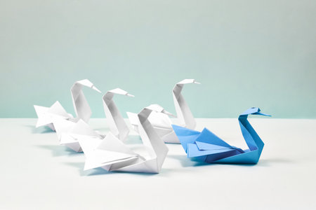 A blue swan leads a flock of white swans. Paper swans on a blue background. Origami. Leadership concept.の写真素材