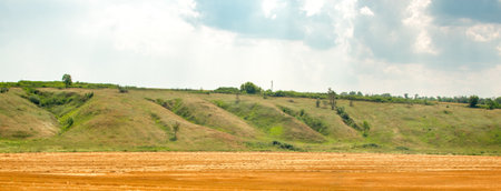 Landscape with hills, beautiful clouds with sunbeams and a sloping wheat field. Selective focus.の写真素材
