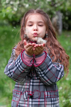Girl blowing on a dandelion in a spring park. Happy child has fun outdoors.の写真素材