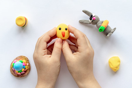 The hands of a small child are holding a yellow plasticine chicken.の写真素材