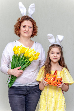 A woman with flowers and a girl with bunny ears and a basket of Easter eggs. The family celebrates...