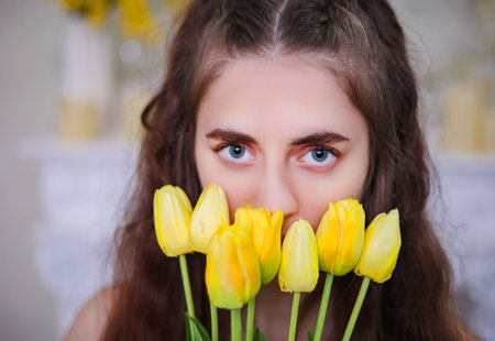 Close-up of a girls eyes with yellow tulips. Spring thoughtful moodの写真素材