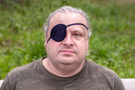 Close-up portrait of a blind, visually impaired man with a black medical patch on his eyeの写真素材