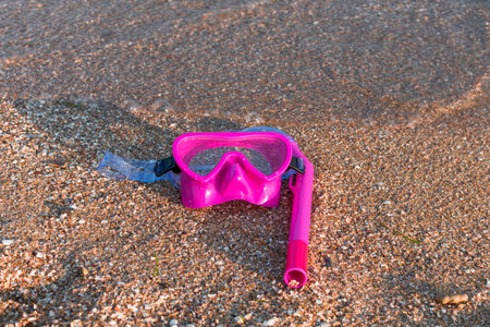 Pink snorkeling gear resting on a sandy beach at the waters edgeの写真素材