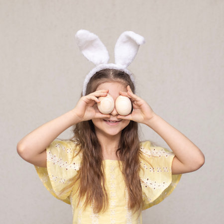 Smiling girl wearing bunny ears holding eggs in a playful pose for Easter
