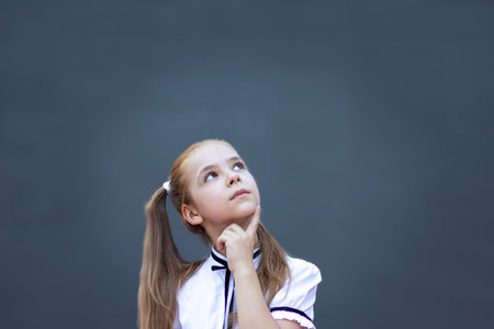 Thoughtful young girl in school uniform reflecting while looking upwards with curiosity