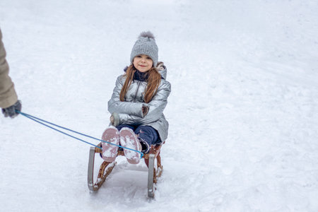 Little girl on a wooden sled being pulled through the snow by a parent in a winter family outing