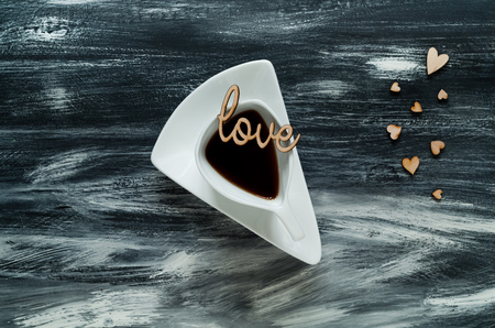 Valentine's day concept, white cup with coffee on small hearts background and love words on blue wooden texture, natural light, space for text, top viewの写真素材