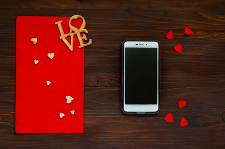 red envelope with hearts and a smartphone on a wooden background, the concept of Valentine's Day, top viewの写真素材