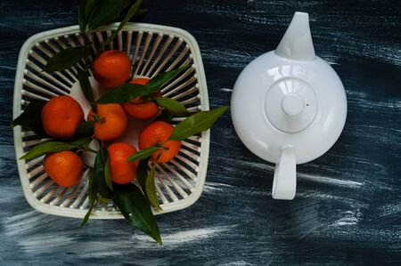 white kettle and mandarins with green leaves in a white authentic vase for fruit on a blue backgroundの写真素材