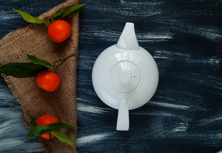 white ceramic teapot and mandarins with green leaves on burlap on a dark wooden backgroundの写真素材