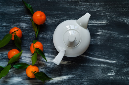 white ceramic teapot and mandarins with green leaves on burlap on a dark wooden backgroundの写真素材