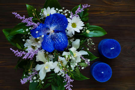 bouquet of spring flowers and blue candles handmade on a wooden background, concept of festive compositionの写真素材