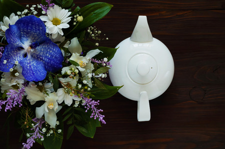 white ceramic teapot and bouquet of spring flowers on a wooden background, concept of festive composition, free space for textの写真素材