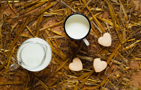 glass jug, mug with milk and cookies in the form of a heart on an organic texture, top view.の写真素材