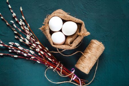 Decor for Easter holidays, a willow branch and decorative colored eggs in burlap on a concrete blue backgroundの写真素材