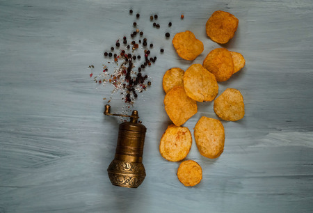 chips and a metal mill for spices on a blue wooden background, top view, space for text. Convenient snackの写真素材
