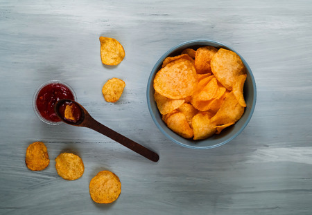 wooden spoon with ketchup and chips in a blue bowl on a blue wooden background, top view, space for text. Convenient snackの写真素材
