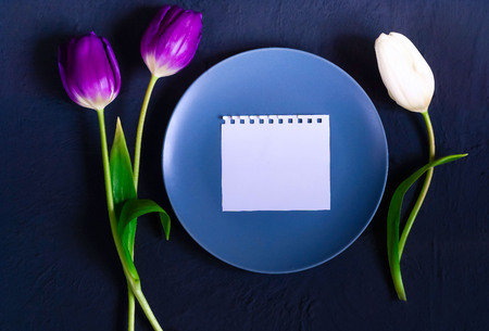blue plate with a note on a blue background of concrete and tulips, top view, space for textの写真素材