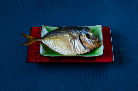 smoked fish on a ceramic plate on a blue concrete background background, top view, space for text