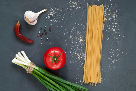 spices and fresh red tomato, ingredients for spaghetti on a dark background, close-up, top view, concept of cooking italian pasta, copy space, minimalismの写真素材