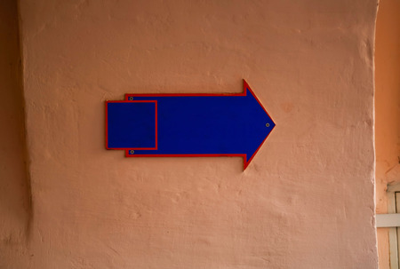 sign in the form of an arrow in blue on a clay light wall, copy space, close-up