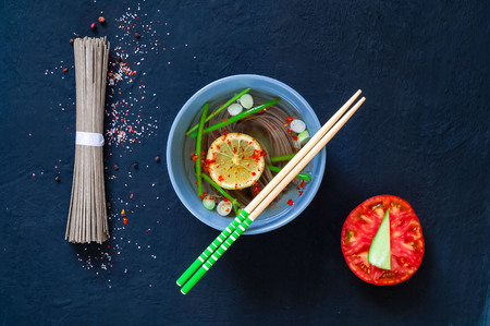 traditional Asian soup of Japanese soba noodles and ingredients on dark background, concept healthy  diet, copy space, closeup.Green neon mood on blue backgroundの写真素材