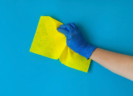 yellow rag for cleaning the house is held by female hand in blue glove on blue background,  natural light, copy space, closeupの写真素材