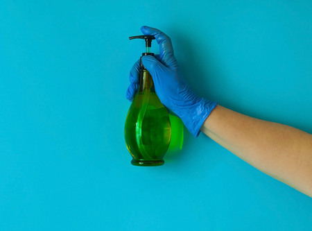 cleanser is held by female hand in blue glove on blue background.The cleanser  is green and the...