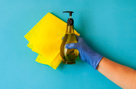 yellow rag for cleaning the house is held by female hand in blue glove on blue background,  natural light, copy space, closeupの写真素材