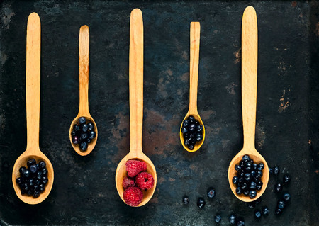 wooden spoons with assorted berries on  background of old rusty metals, concept of organic food,...