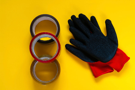red gloves  and  colored scotch tape, Accessories for packaging on yellow background,copy space,...