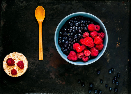 bilberry and raspberries in blue bowl, the concept of organic berries bowl  on vintage rusty metal background. . Berry picking, copy space, close up, bannerの写真素材