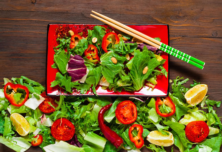 Salmon Poke Salad on red plate with chopsticks on Organic Texture from Salad Leaves on Wooden Background, tasty and healthy meal,detox food or vegetarian concept. Top view, copy space, flat lay.の写真素材
