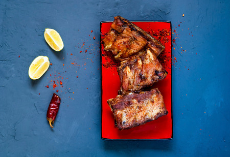 Spicy hot grilled spare ribs from BBQ served with  hot chili pepper and lime in red ceramic dish on...