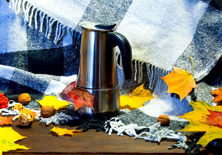 Autumn home decor.Metallic coffee pot  amid bright yellow leaves on the background of knitted clothes and checkered plaid.の写真素材