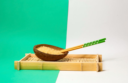 Rice in organic coconut bowl with chopsticks on geometric paper background. Yellow and turquoise trendy colors, close up,copy spaceの写真素材