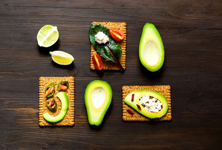 Plated avocado toast with delicious toppings goat cheese and chard lettuce on wooden background.The...