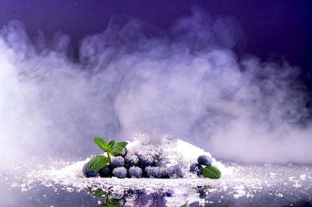 Blueberries on background of snow and smoke. Purple fashionable color.Holiday and celebration...