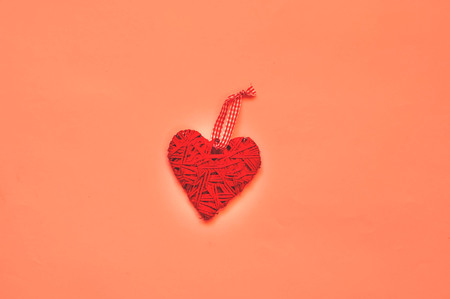 Valentines Day concept. Creative paper background with wicker heart. Living Coral trendy color.Holiday concept for postcard or invitation. Top view, copy space, closeup.の写真素材