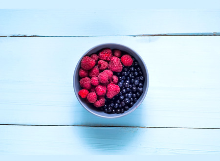Raspberry and blueberry in blue bowl on light wooden background. Berry picking, organic food...