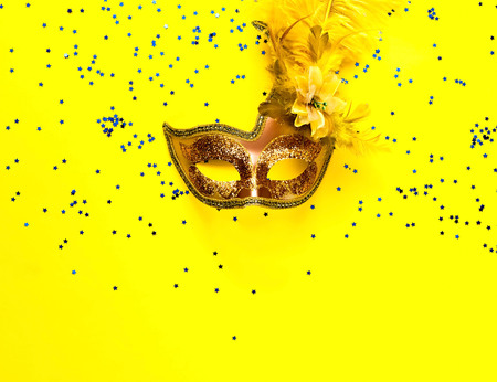 Carnival mask on yellow background with sparkles. Festive backdrop for projects. Flat lay, close up. Top view, copy space.の写真素材