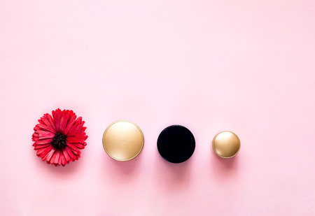 Festive background for decorative cosmetics with gerbera flower. Cosmetic creams in jars with gold lids on pastel pink background. Close, copy space.の写真素材