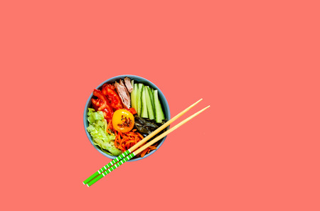 Traditional dish of Korean cuisine. Bibimbap with beef, vegetables and egg on coral background. Top view. Closeup, copy space.の写真素材