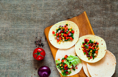Traditional dish of Mexican cuisine. Corn tortilla tacos with vegetable filling on  burlap texture....