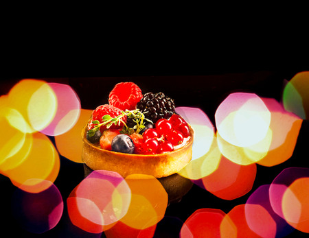 Cupcake and berries with reflection on black background with blur effect. Food concept, colorful...