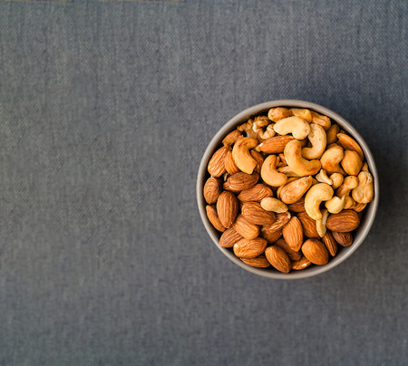 Healthy breakfast. Cashews and almonds in blue bowl on gray background. Closeup, copy space.の写真素材