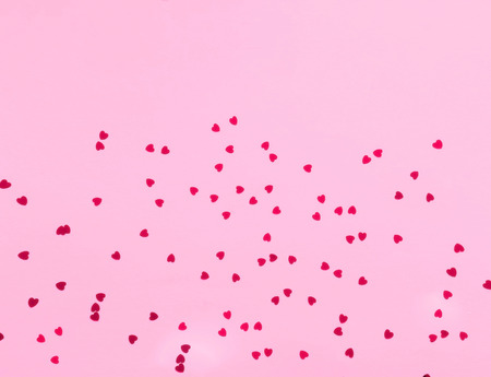 Festive pink background with spangles in the shape of heart.Closeup, copy space.