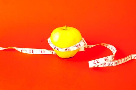 Apple with centimeter tape on orange background. Healthy eating concept. Close-up, copy spaceの写真素材